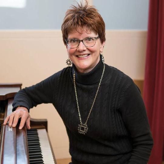 woman with glasses sitting at piano